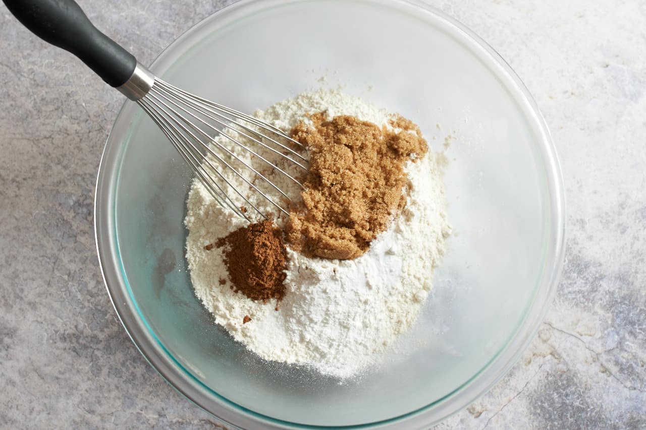 A whisk in a bowl with flour, pumpkin pie spice and other dry ingredients.