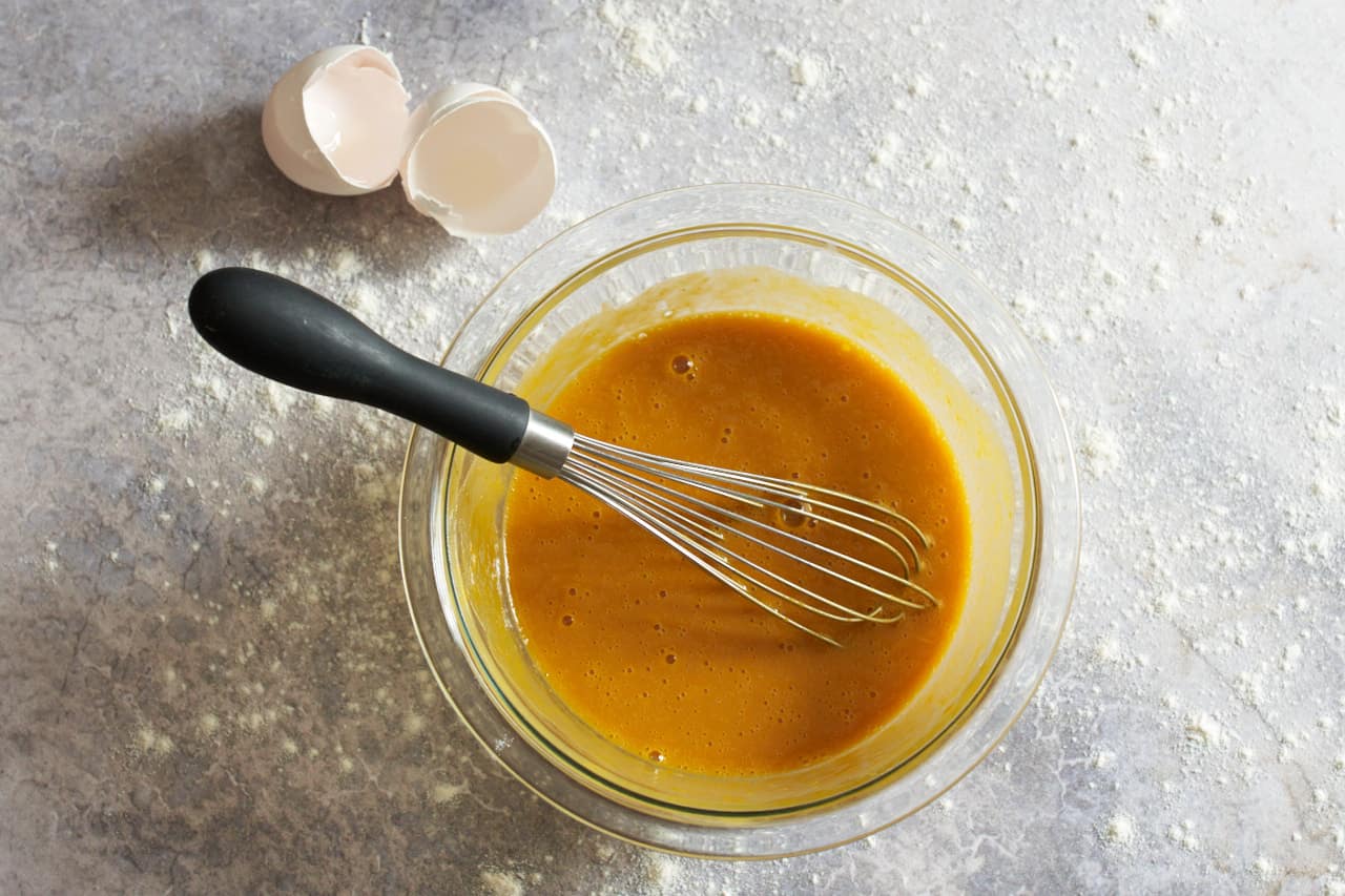 A whisk in a bowl of pumpkin puree blended with eggs.