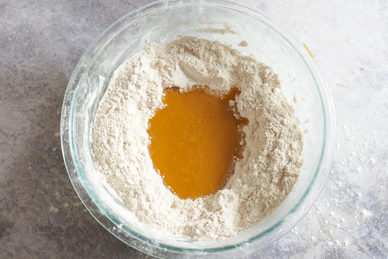 Pumpkin puree mixture poured into a well in the center of a bowl of flour.