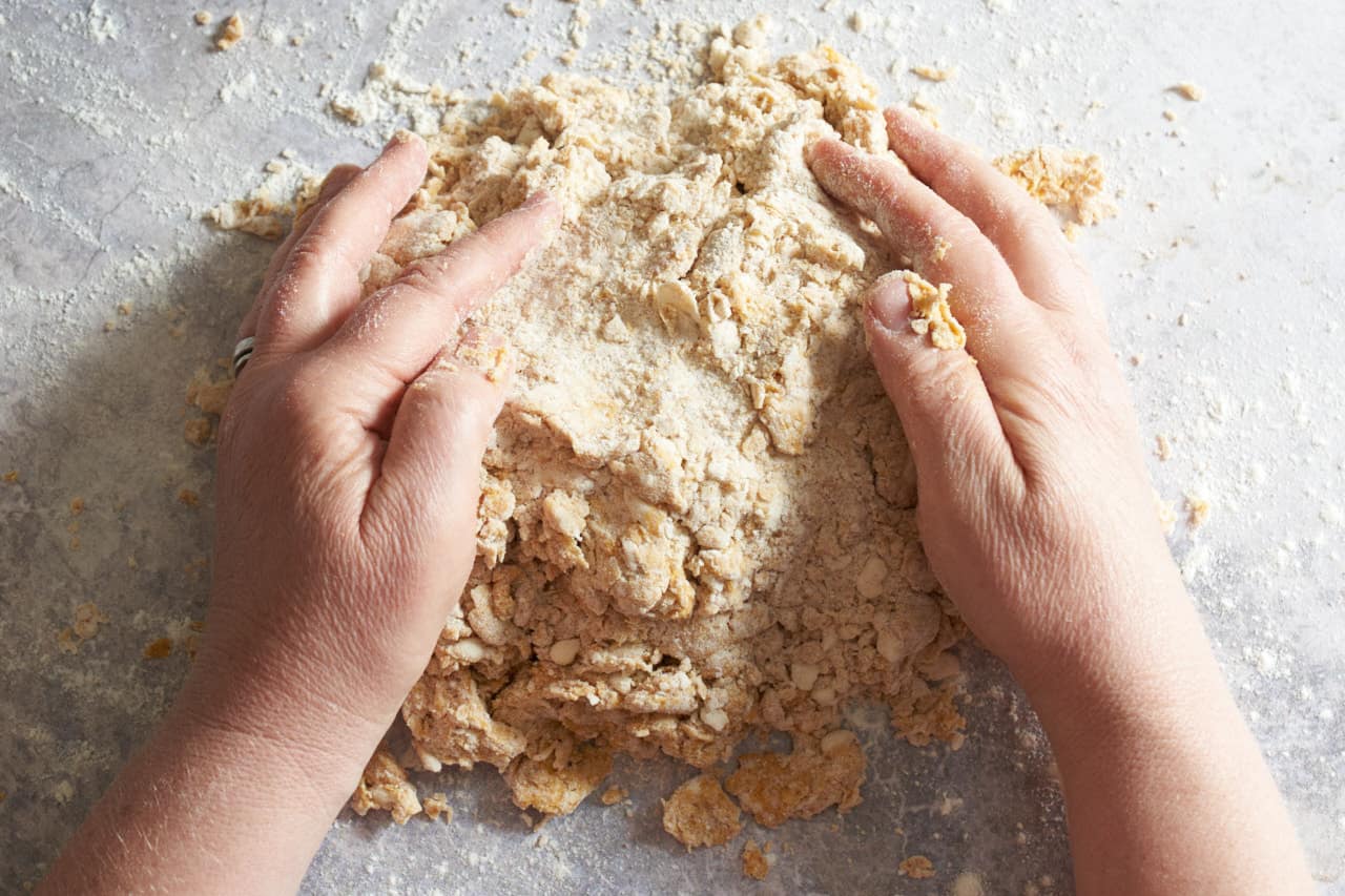 A woman's hands shaping pumpkin scone dough before cutting it.