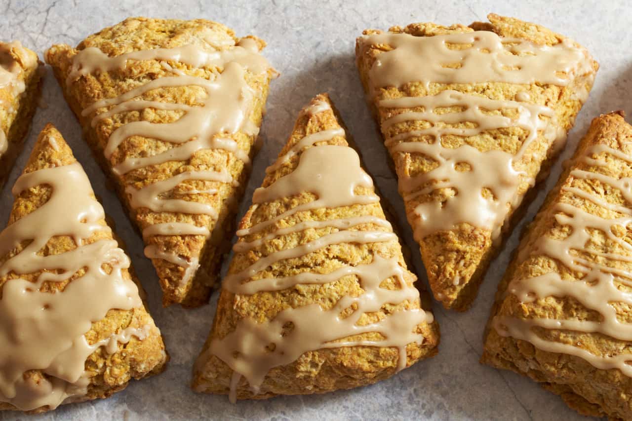 Pumpkin scones with maple glaze lined up on a gray surface.