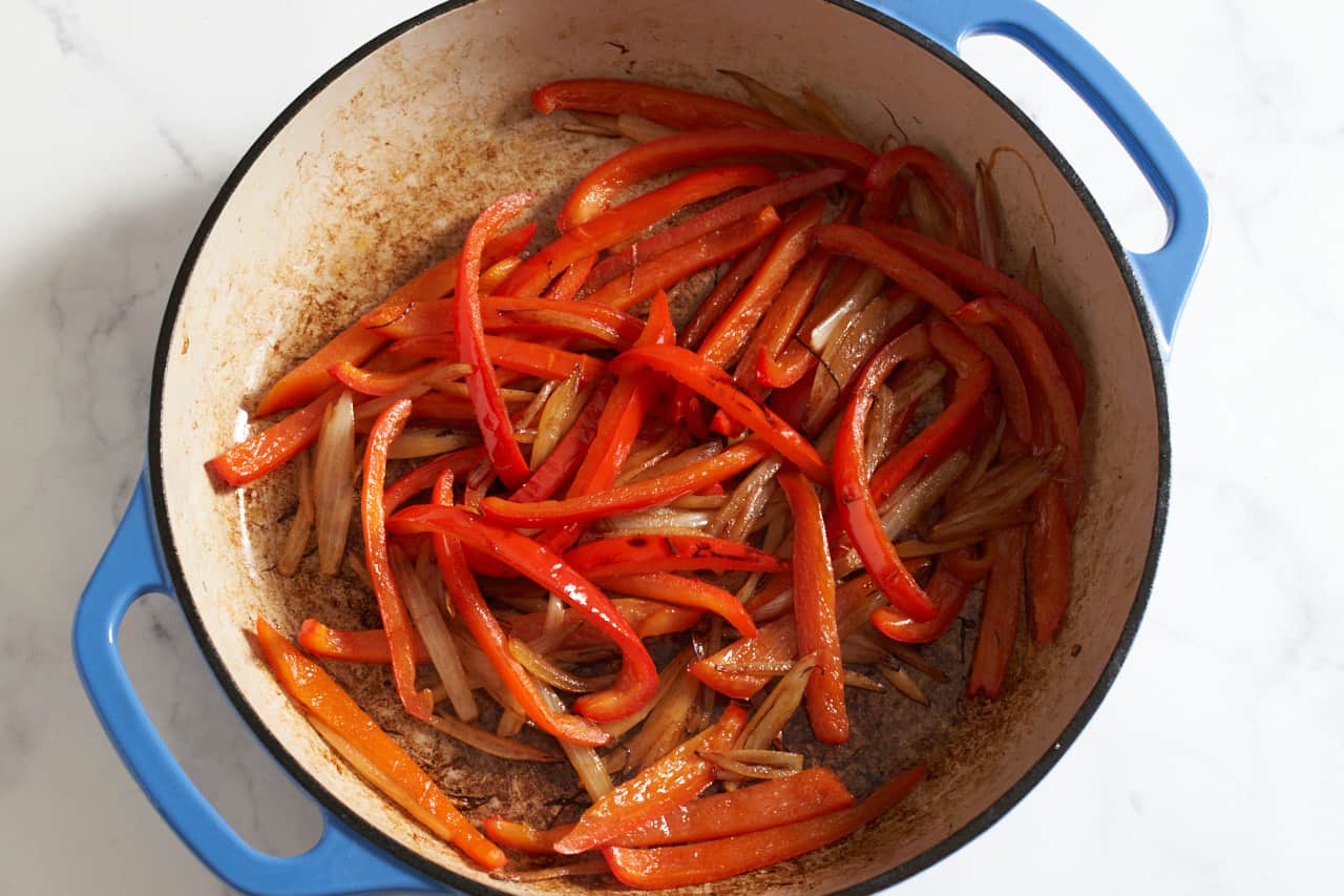 Sautéed red bell peppers and onions in a blue pan.