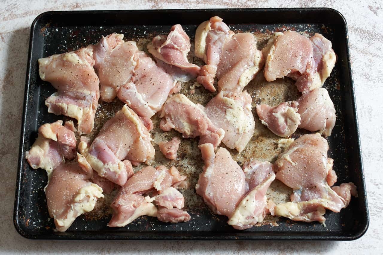 Raw chicken thighs seasoned with salt and pepper on a sheet pan.