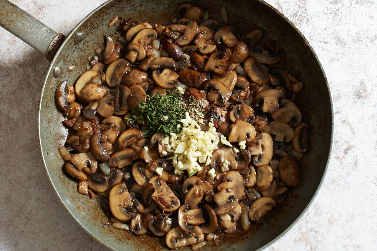 Cooked mushrooms in a skillet with diced garlic and chopped rosemary added.