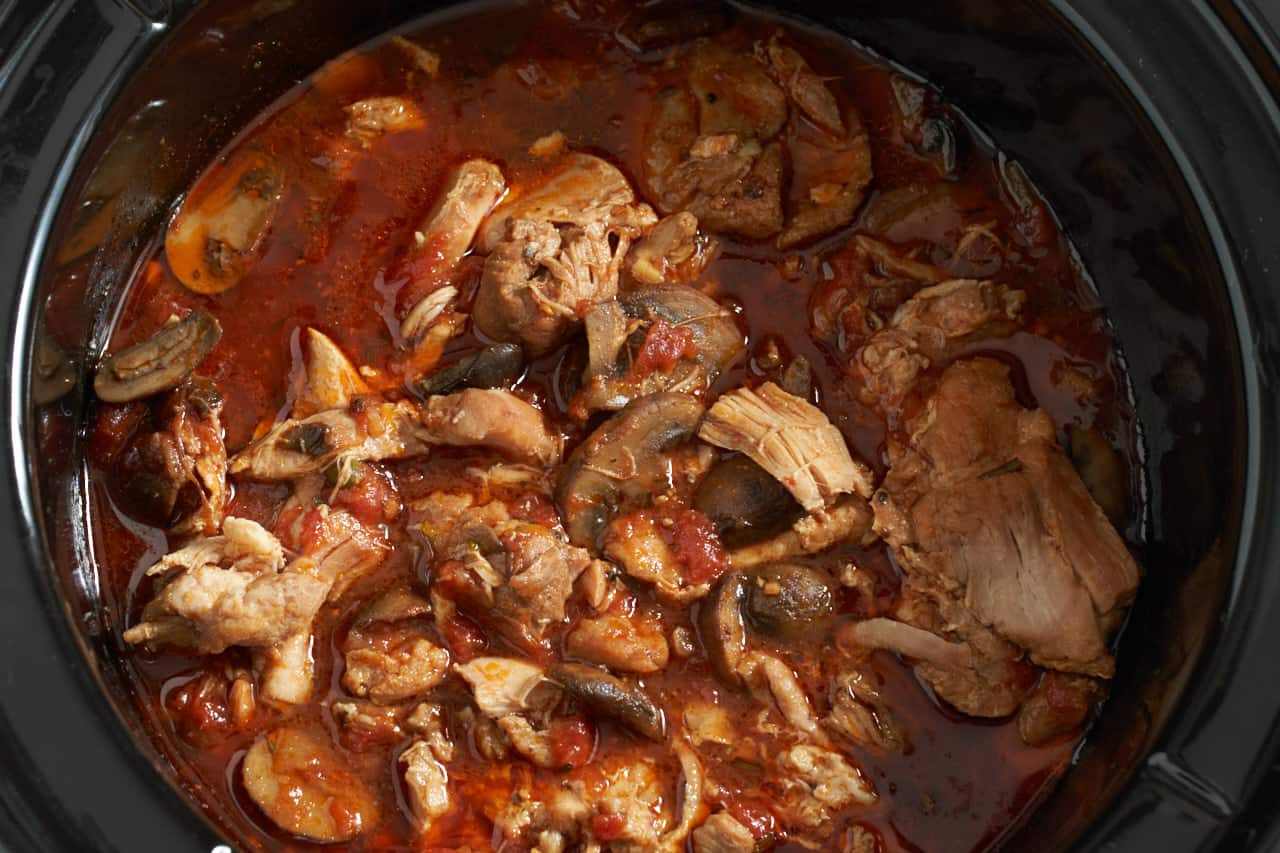 Finished chicken cacciatore in a black slow cooker.