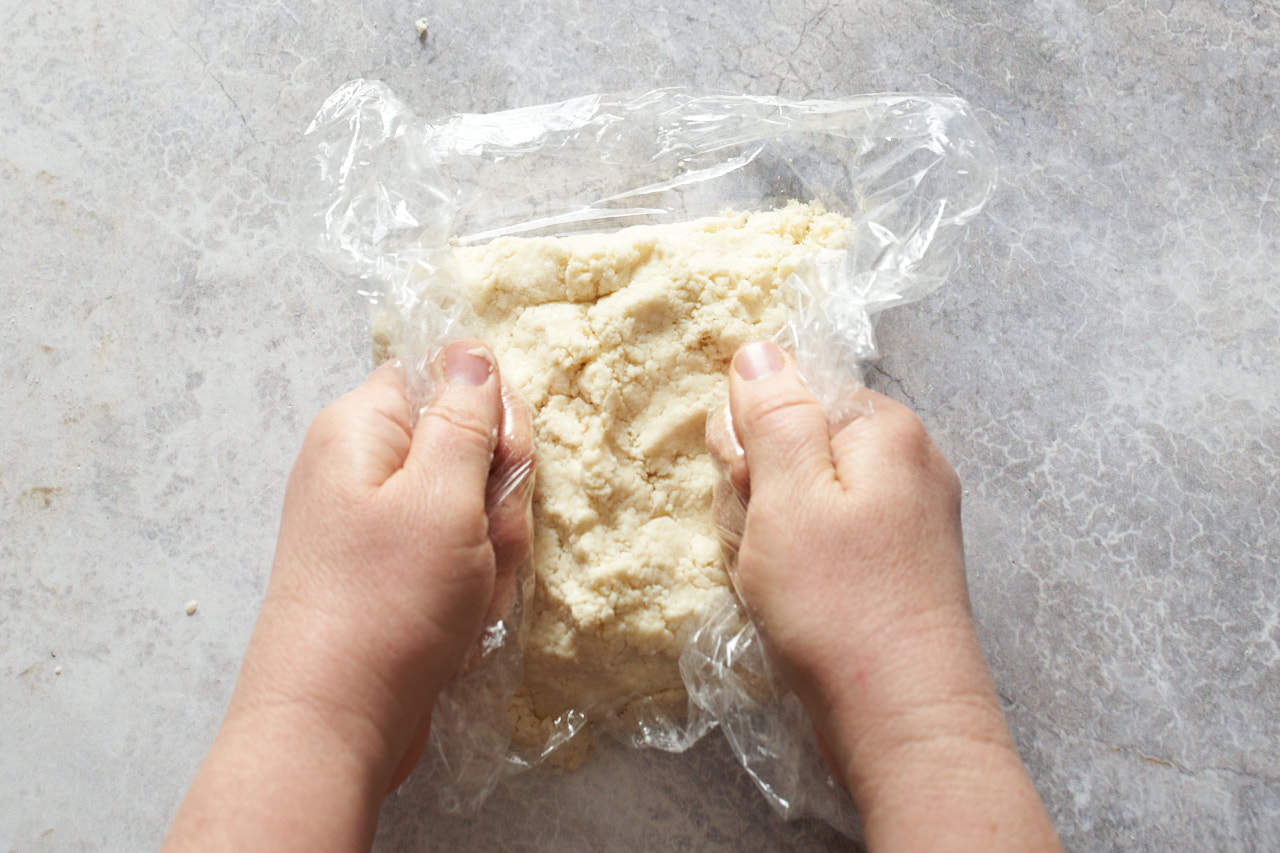 A woman's hands compressing galette crust into a disc in a piece of plastic wrap.