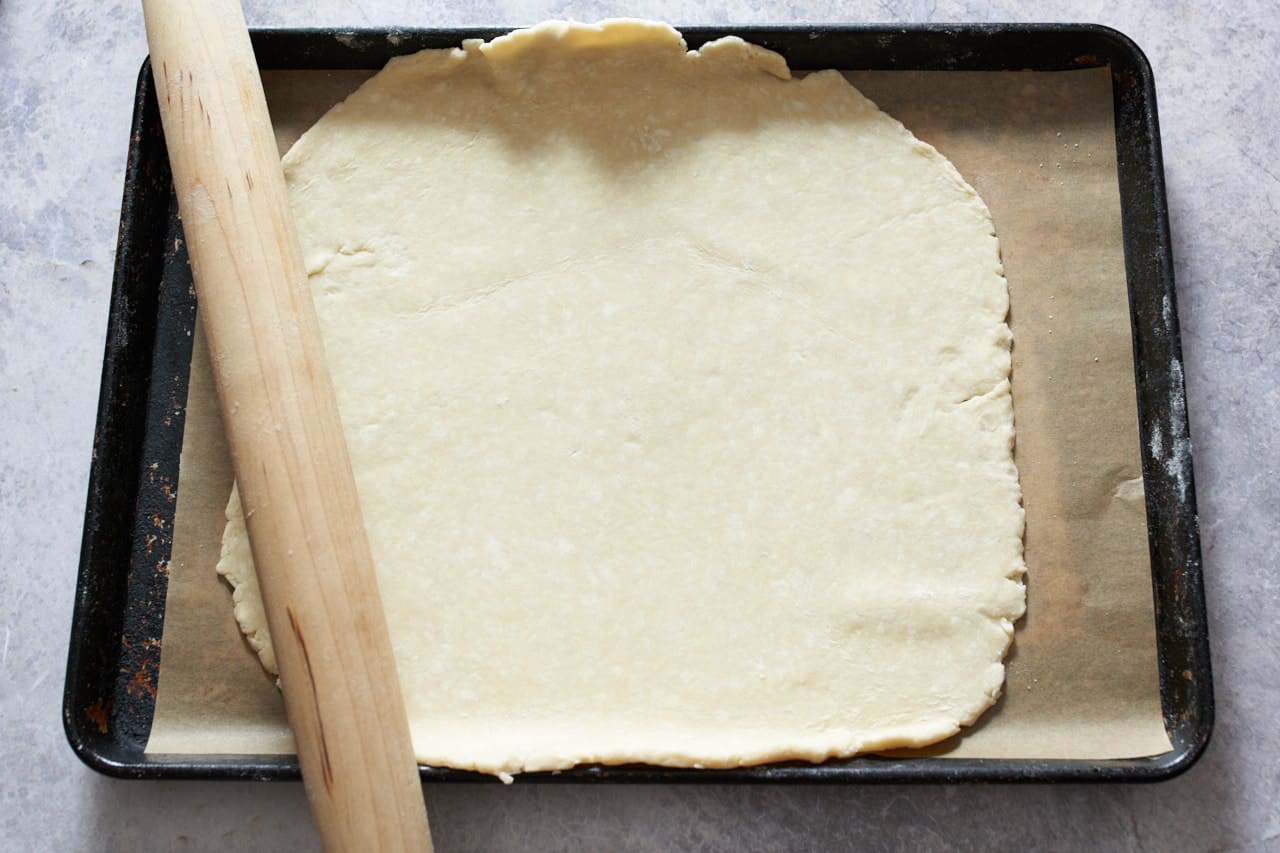 Galette crust rolled out and placed on a sheet pan lined with parchment paper. A rolling pin is on the left.