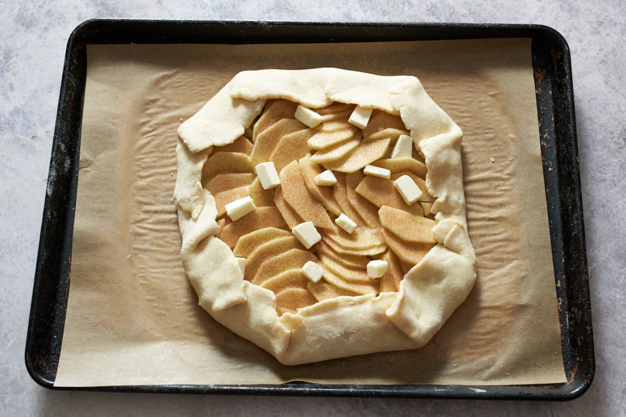 An apple galette with small pieces of butter on top ready to go into the oven.