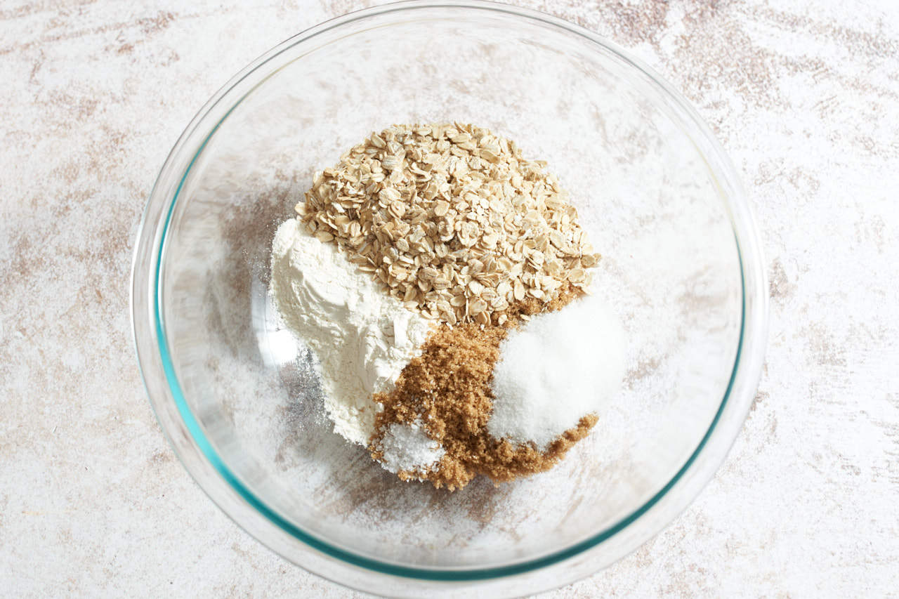 A glass bowl of oats, flour, brown sugar, granulated sugar, and salt.