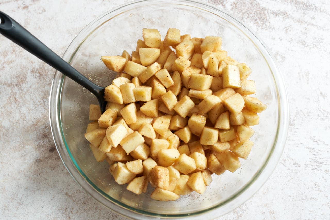 A bowl of cubed apples tossed in brown sugar, cinnamon and nutmeg.