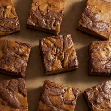 Nine pumpkin brownies with a chocolate swirl on top arranged on brown parchment paper.