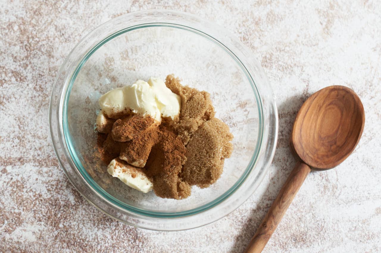 A glass bowl of softened butter, brown sugar, and spices, with a wooden spoon next to it.