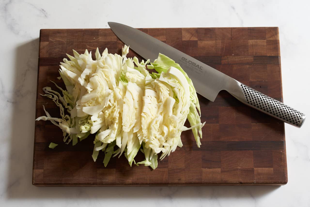 A knife on a cutting board with sliced cabbage.