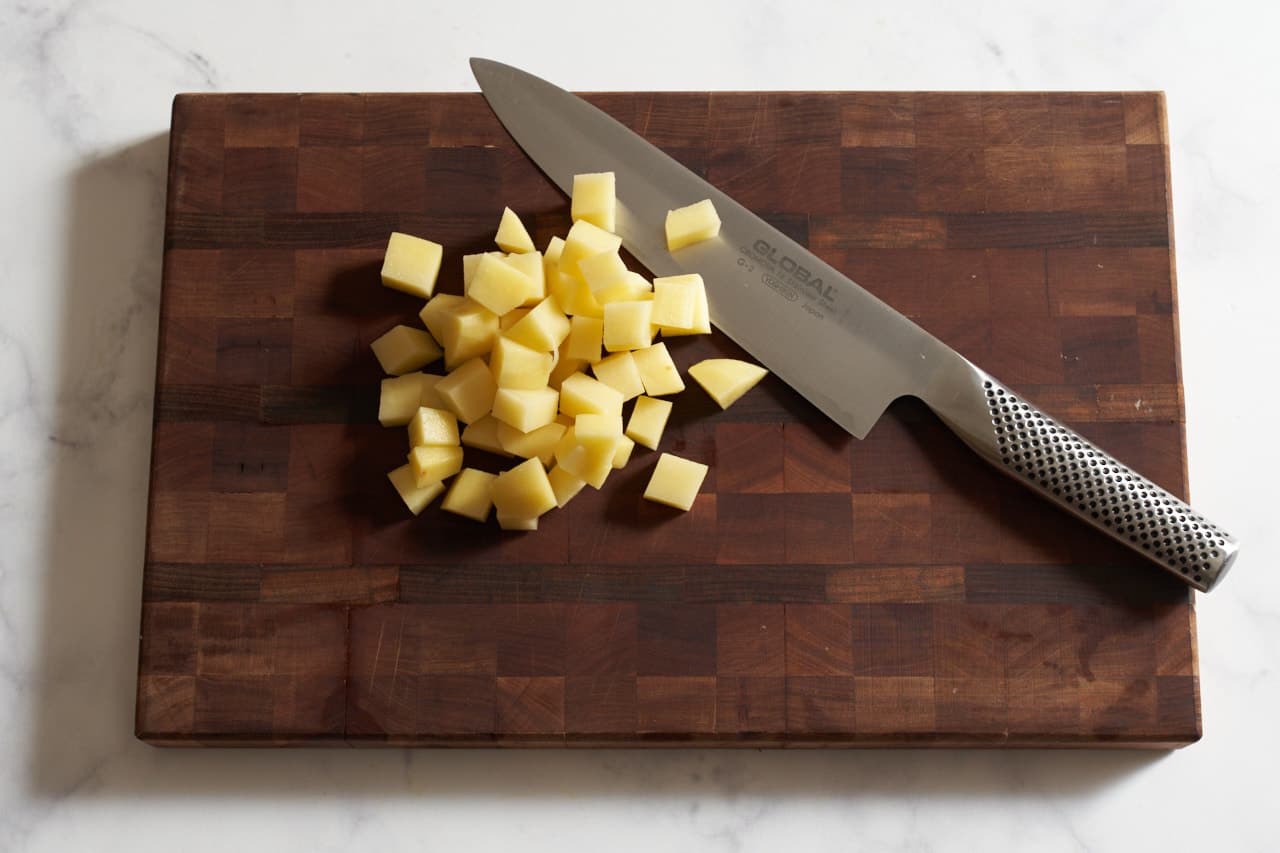 A knife on a cutting board with diced potatoes.