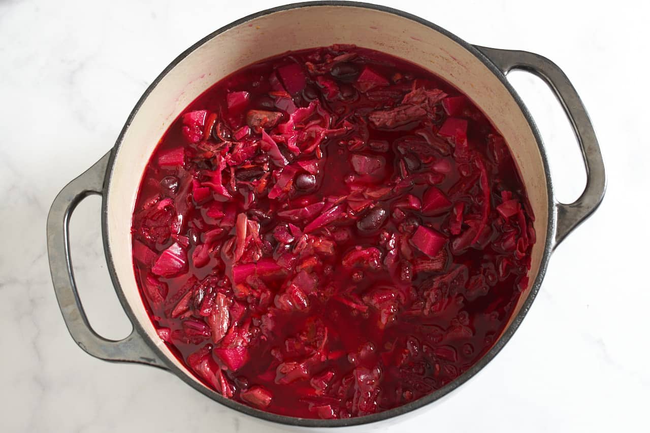 Finished borscht in a Dutch oven, it has turned a bright pinkish-purple color throughout.