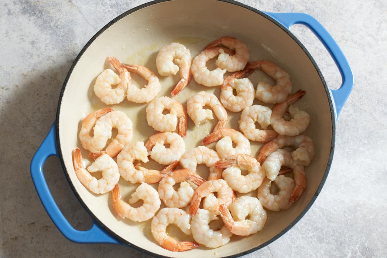 Shrimp cooking in a pan with blue handles.