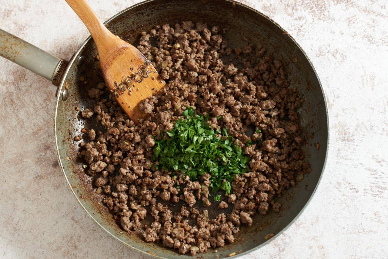 Cooked ground lamb in a skillet topped with fresh chopped parsley.