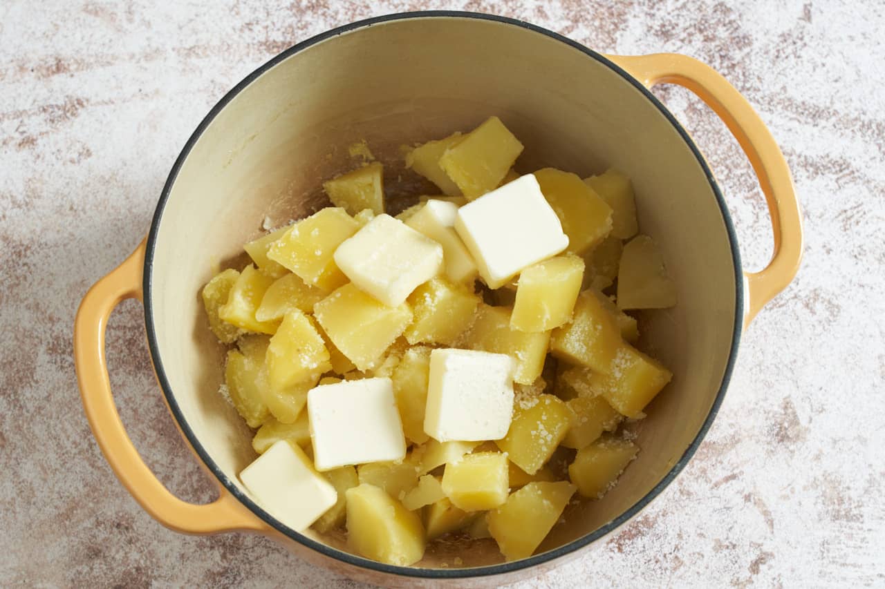 Cooked potatoes in a pot with several pats of butter.