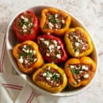 Greek stuffed peppers topped with feta and parsley in an oval baking dish.