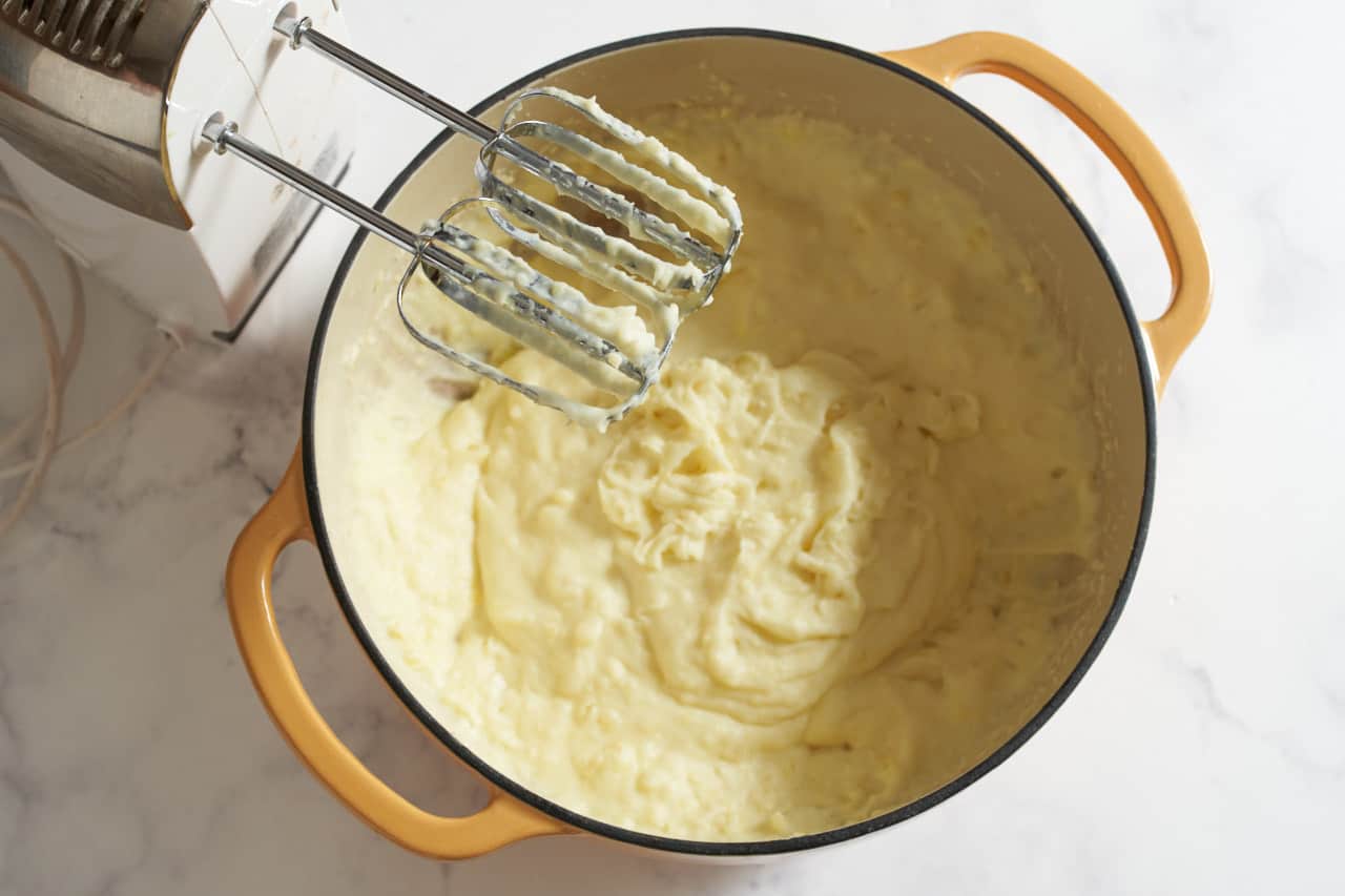 The beaters of a hand mixer over a pot of mashed potatoes.