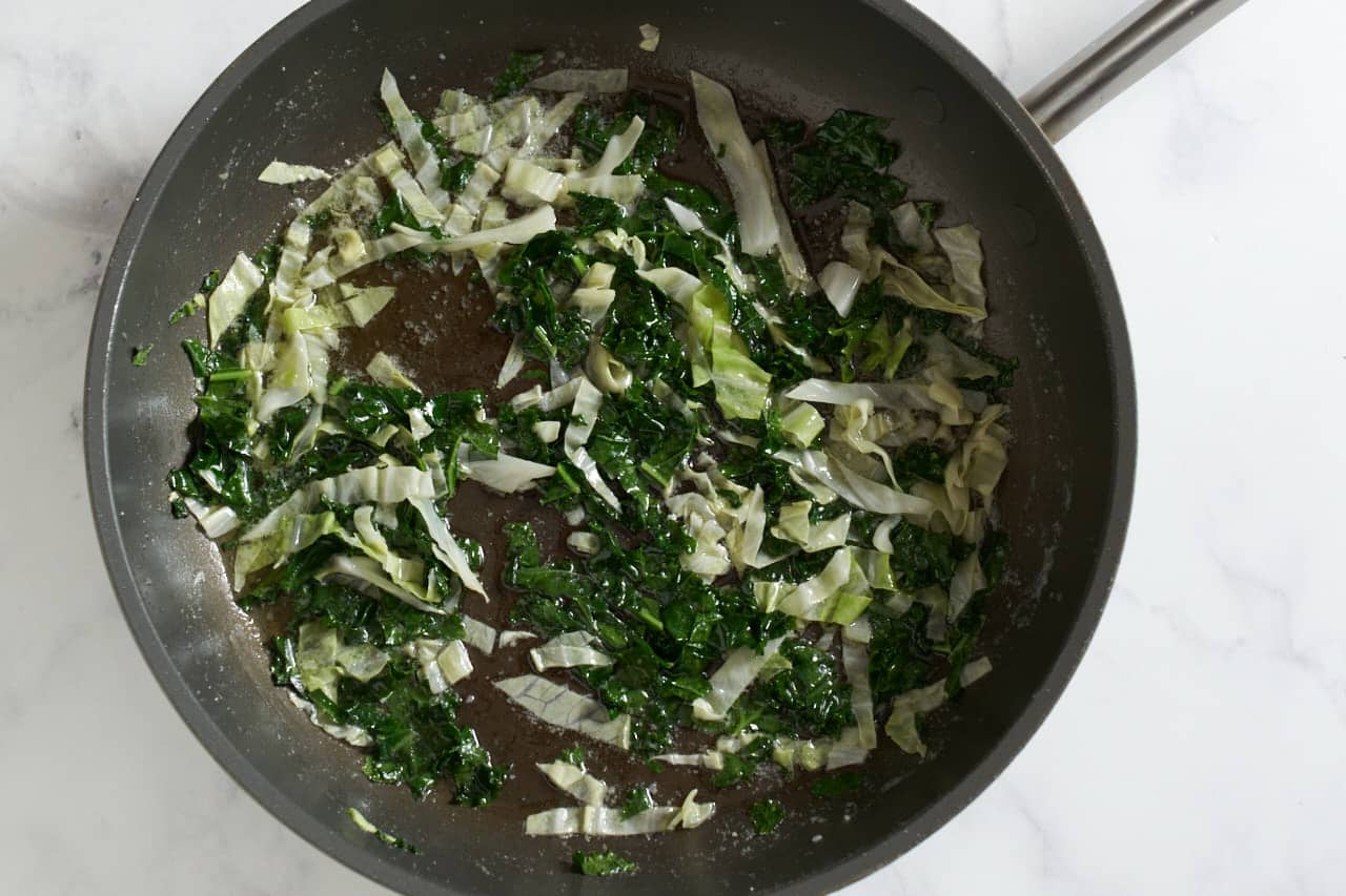 Kale and cabbage cooking in butter in a skillet.