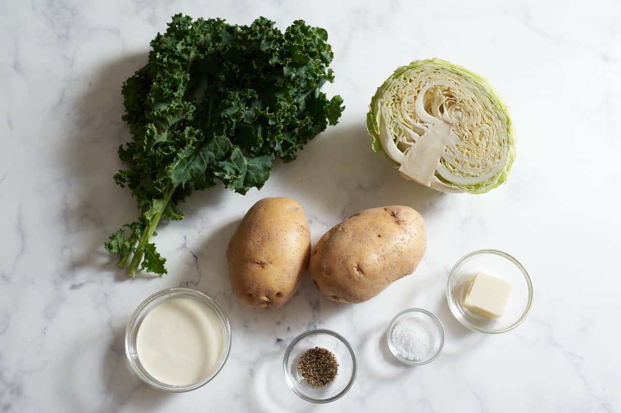 Fresh kale, half a head of cabbage, two potatoes, and small bowls of cream, butter, salt, and pepper.