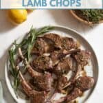 Pan seared lamb chops on a white plate with fresh sprigs of rosemary. Fresh lemons and a bowl with herbs and garlic, are above it, a green towel is on the left.