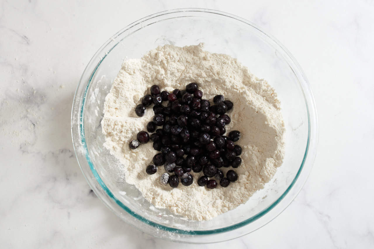 Blueberries in a bowl of flour and other dry ingredients that has had butter cut into it.