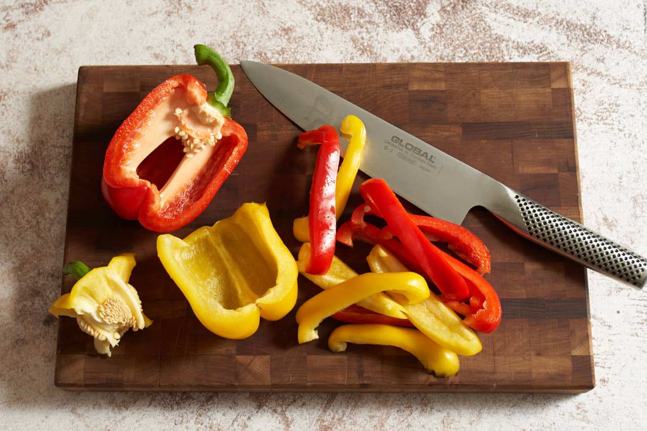 A knife on a cutting board with sliced red and yellow bell peppers.