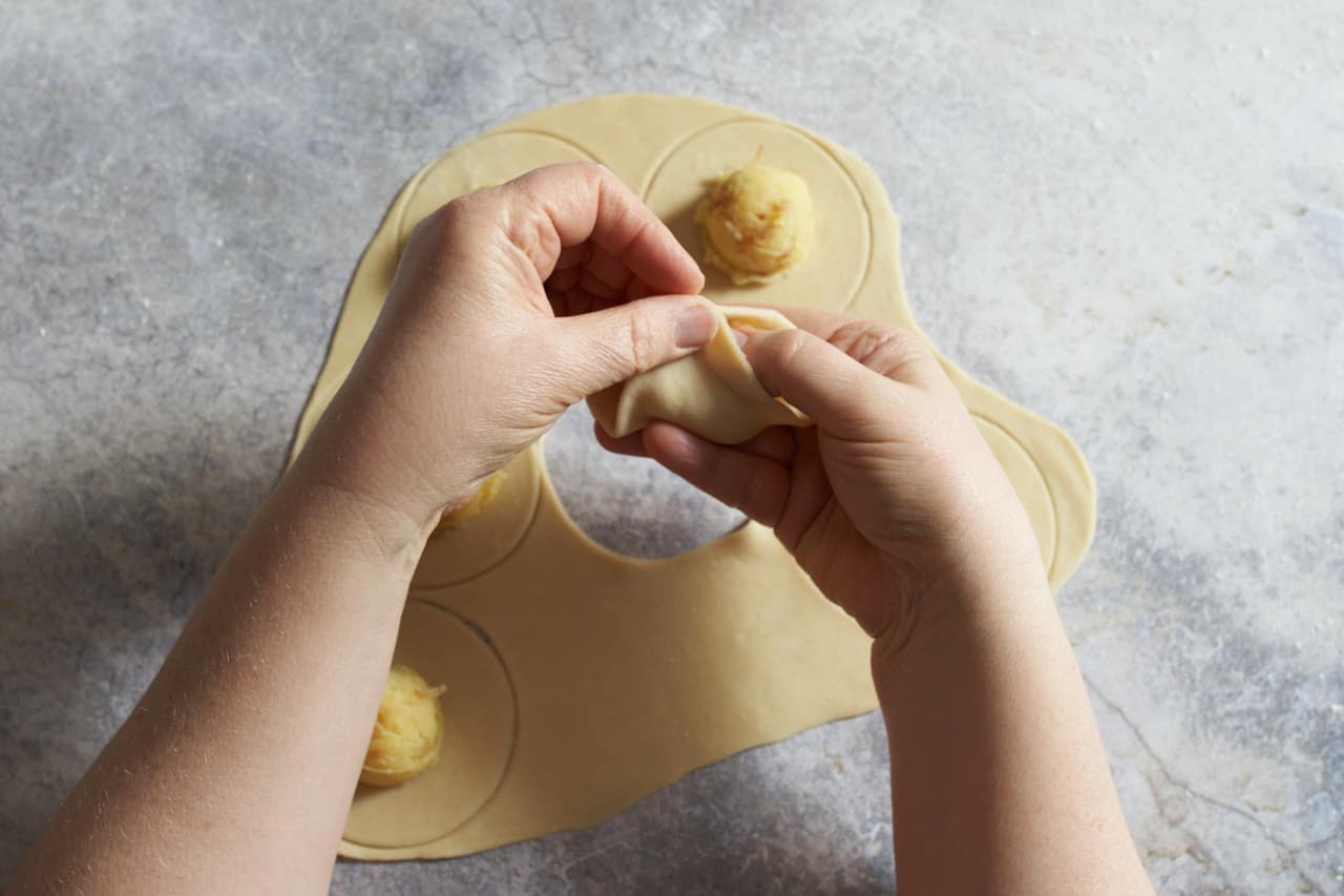 A woman's hands folding a Ukrainian potato dumpling.