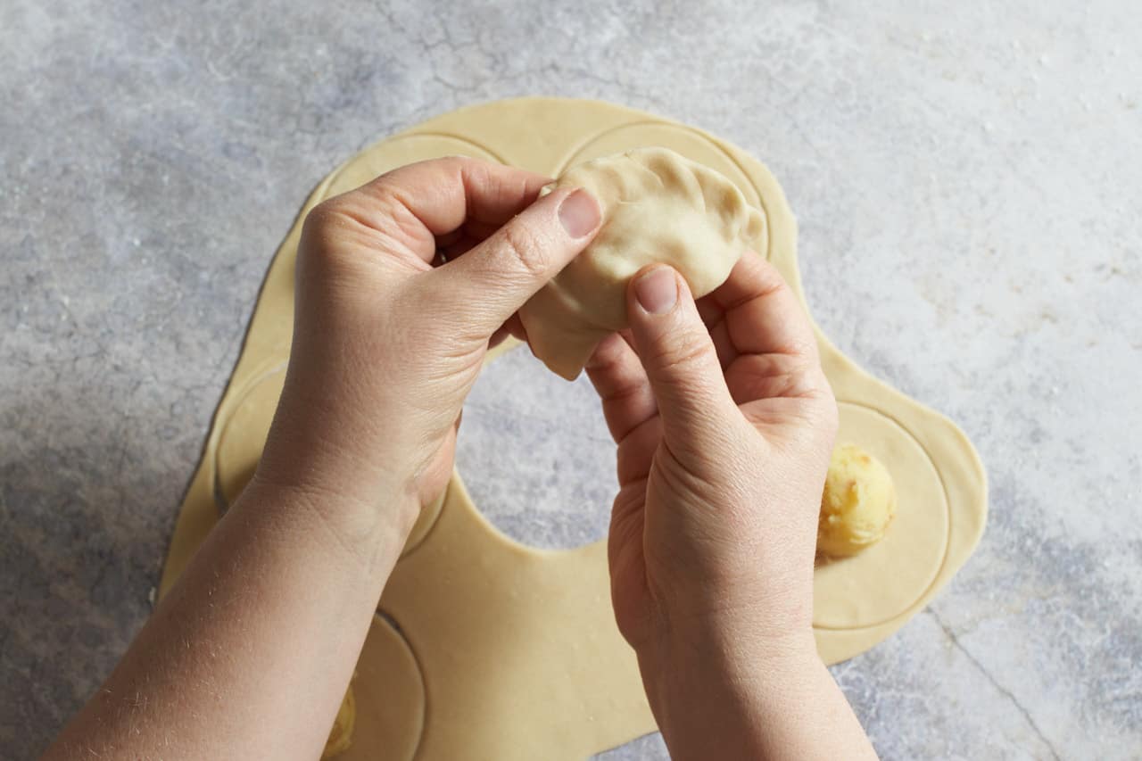 A woman's hands shown pinching the edges of a Ukrainian potato dumpling to close it.