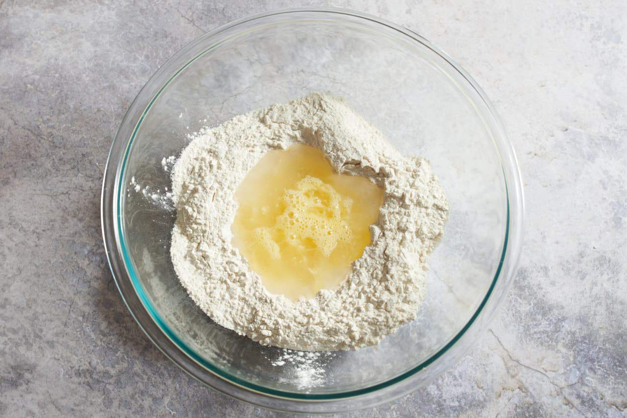 A bowl of flour with a well of liquid in the center.