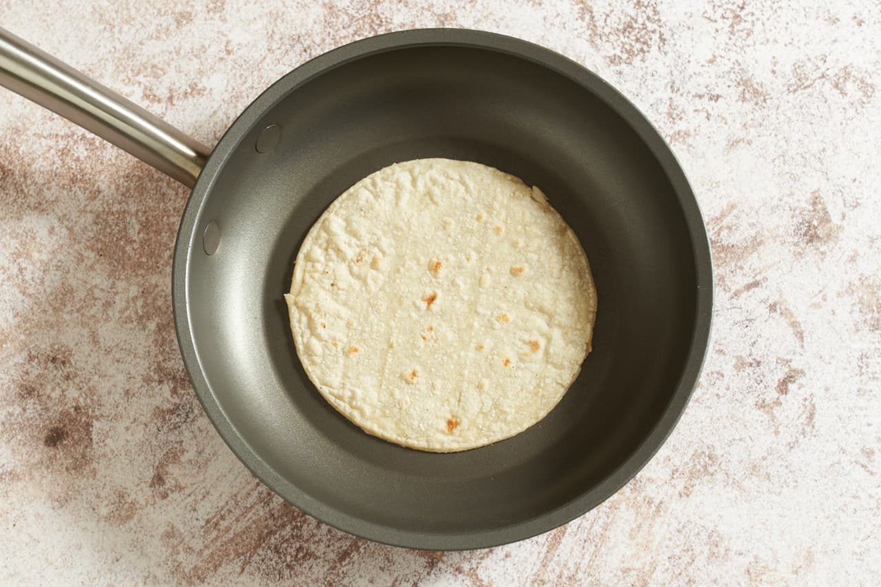 A corn tortilla in a non-stick skillet.