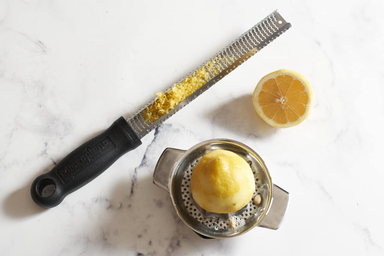 A microplane grater with lemon zest, and a small juicer with half a lemon on it.