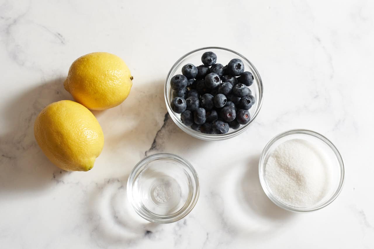 Two lemons, and small bowls of blueberries, sugar, and water.