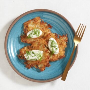 Ukrainian potato pancakes (deruny) topped with sour cream and dill on a blue plate, a gold fork is on the right.