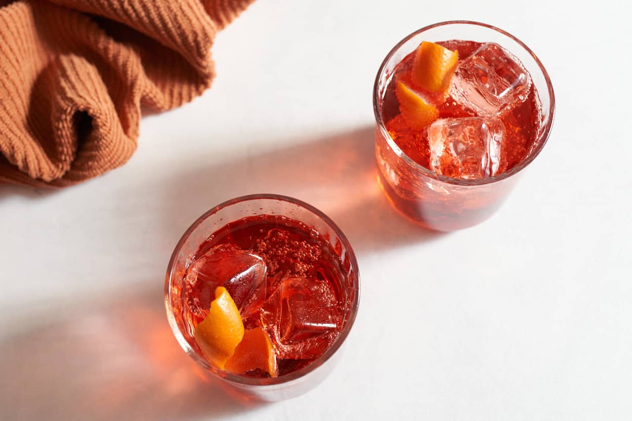 Two Americano cocktails garnished with orange twists next to an orange towel.