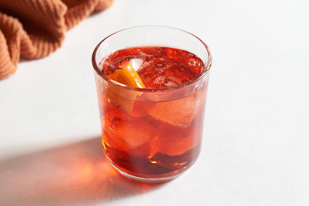 An Americano cocktail garnished with orange twists next to an orange towel.