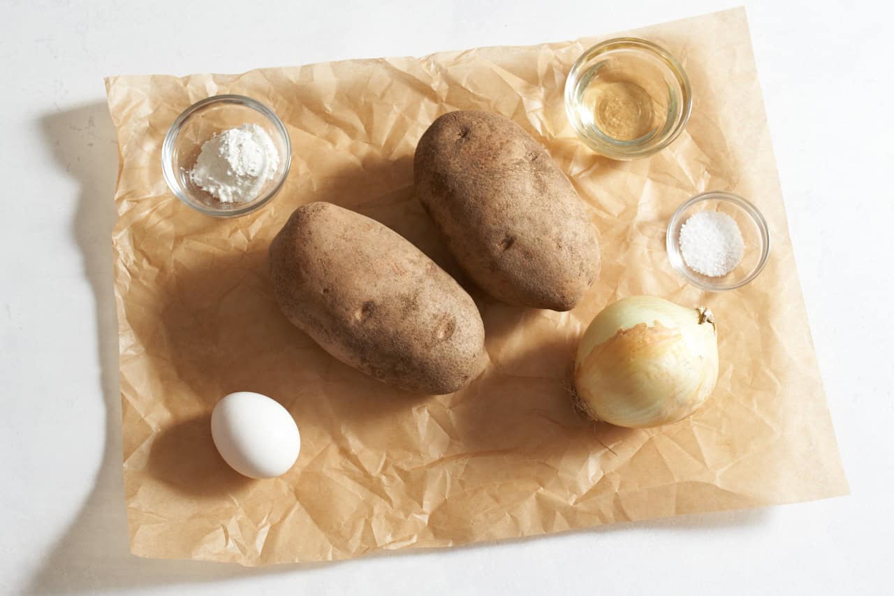 Two potatoes, an onion, an egg, and small bowls of corn starch, salt, and sunflower oil.