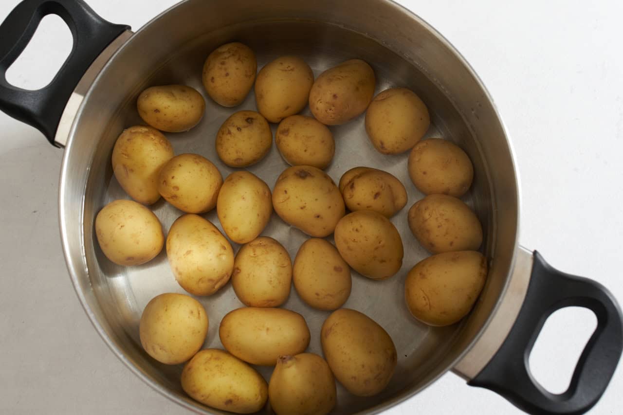 A deep pot full of small potatoes covered in water.