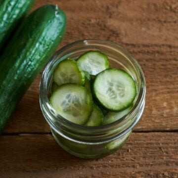 A small jar of quick pickles, two cucumbers are on the left.