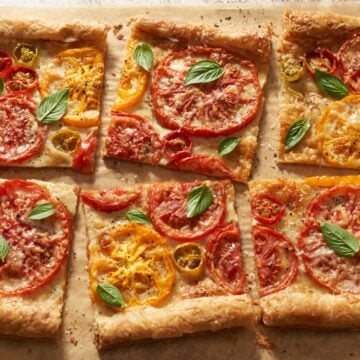 A puff pastry tomato tart topped with fresh basil and sliced into squares.