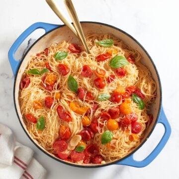 Cherry tomato pasta with garlic topped with fresh basil in a pan with blue handles.