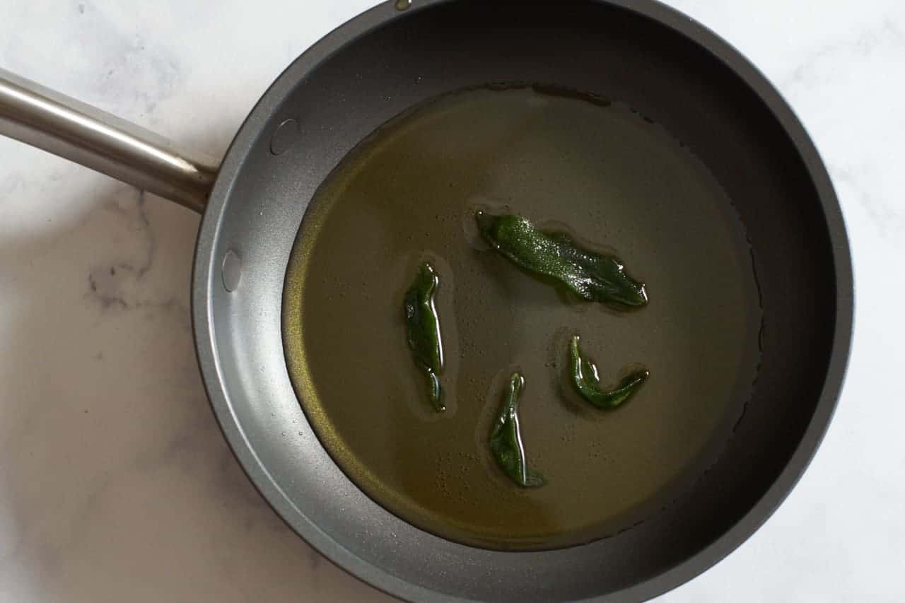 Sage leaves frying in olive oil in a small skillet.