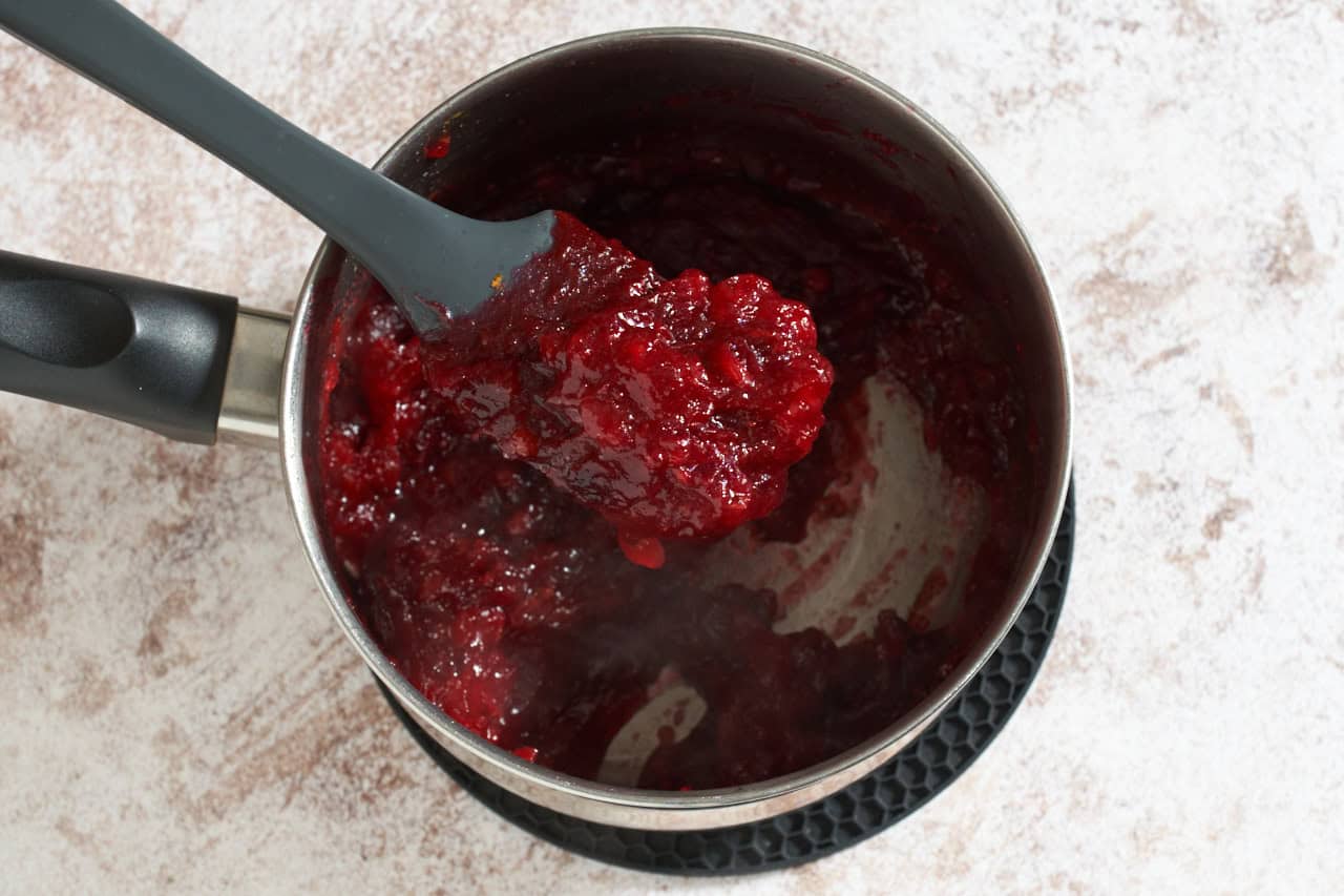 A spatula full of cooked down cranberry compote over a sauce pan.