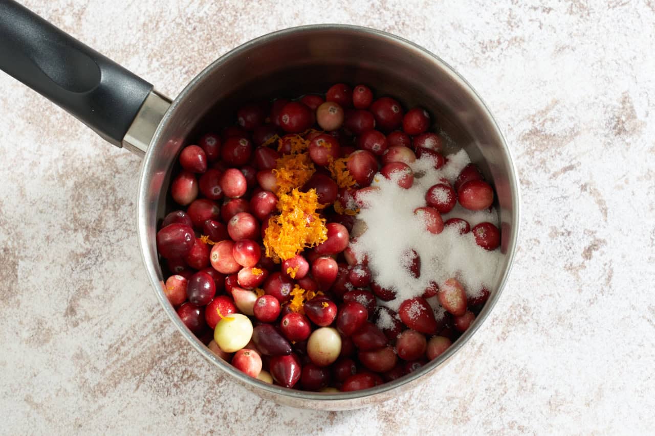 A sauce pan with fresh cranberries, orange juice, orange zest and sugar.