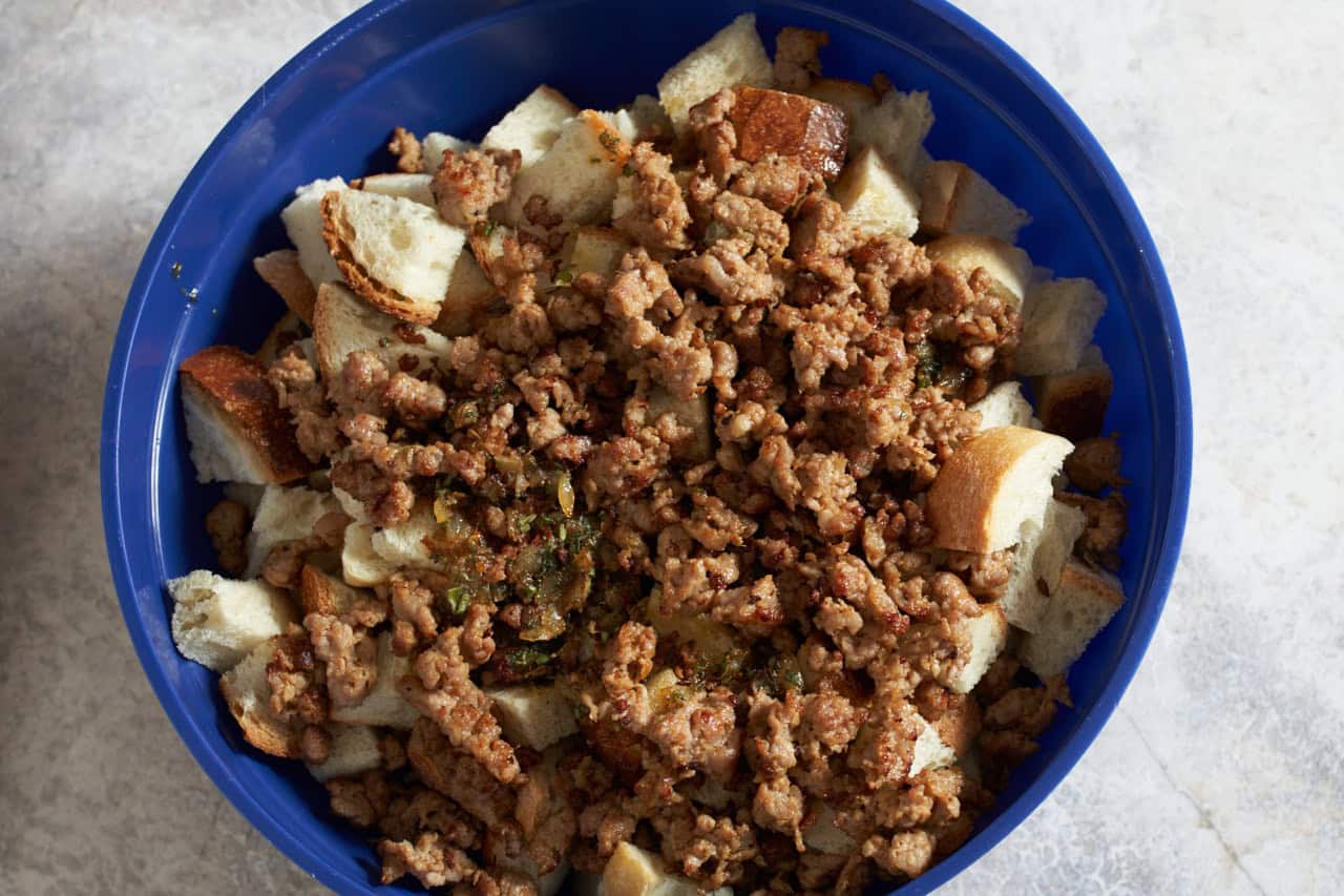 Stuffing cubes topped with Italian sausage in a large blue bowl.