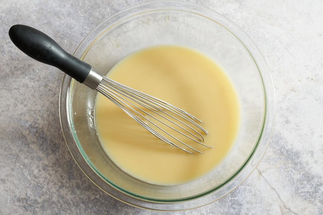 A whisk in a glass bowl of chicken stock with beaten eggs in it.