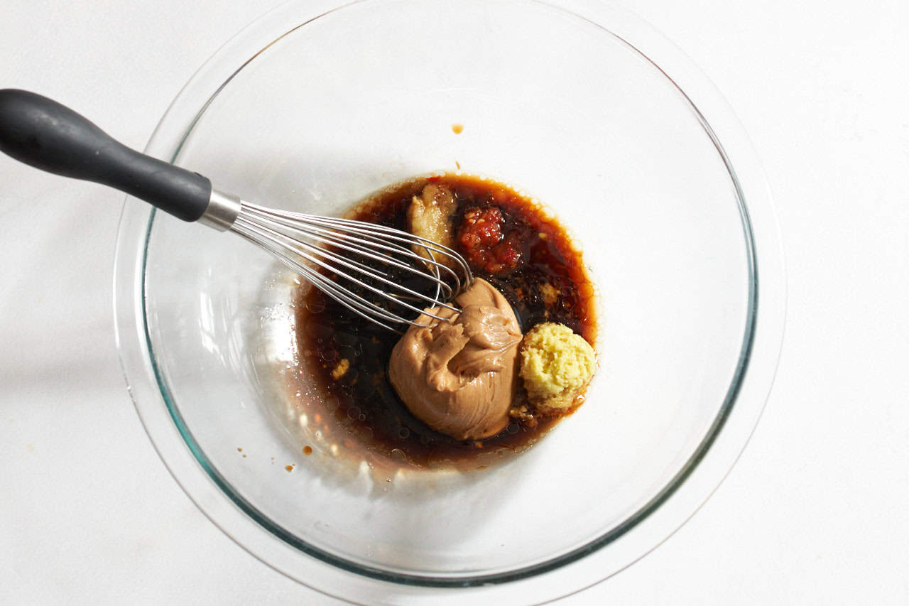 Ingredients for spicy peanut sauce in a glass bowl with a whisk.