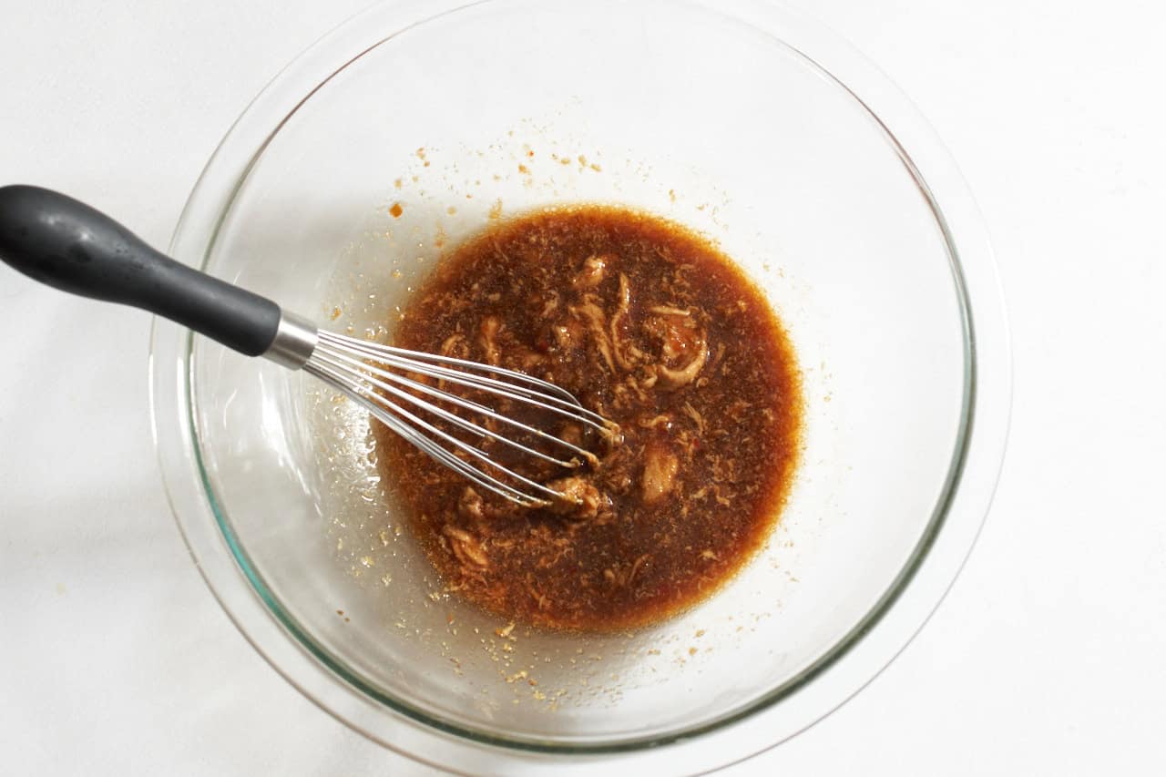 Peanut butter being stirred into soy sauce and other ingredients with a whisk.